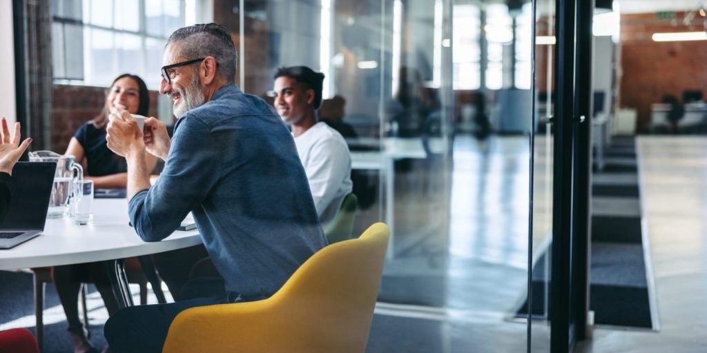Cheerful mature businessman attending a meeting with his colleagues in an office. Experienced businessman smiling while sitting with his team in a meeting room. Creative businesspeople working together.