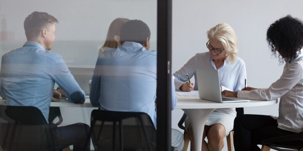 Multi-ethnic business people accomplish important negotiations with contract signing, company representatives and client sitting behind closed doors at modern boardroom, view through the glass wall